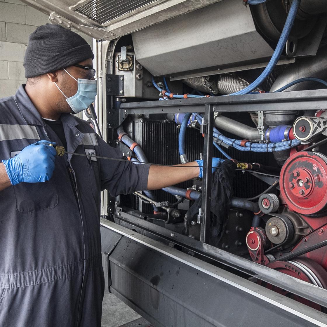 Mechanic with mask on, checking engine oil